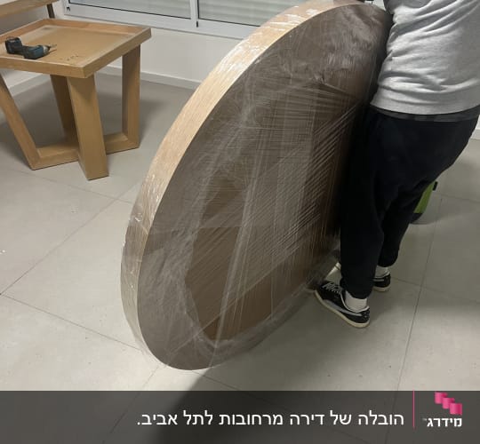 אדם מחזיק שולחן עגול עטוף בניילון